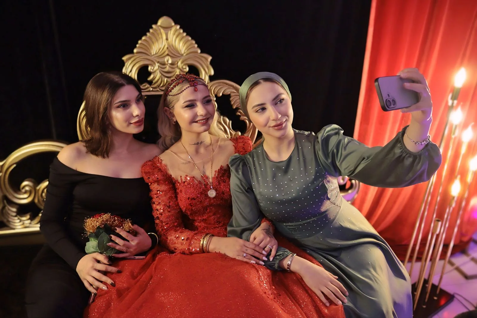 Altın işlemeli kına tahtında kırmızı elbiseli gelin ve arkadaşları hatıra fotoğrafı çektirirken